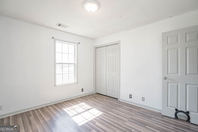 unfurnished bedroom with a textured ceiling, light hardwood / wood-style flooring, and a closet