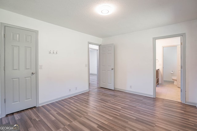 unfurnished bedroom featuring connected bathroom, a textured ceiling, and dark wood-type flooring