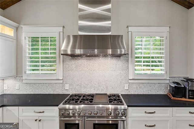 kitchen with tasteful backsplash, white cabinets, wall chimney range hood, vaulted ceiling with beams, and double oven range