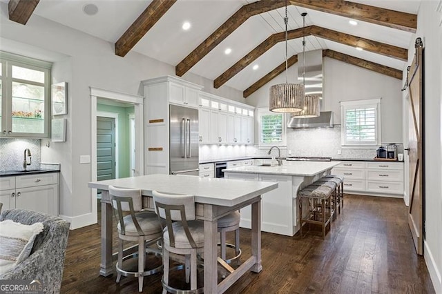 kitchen featuring pendant lighting, beamed ceiling, a kitchen island with sink, backsplash, and appliances with stainless steel finishes