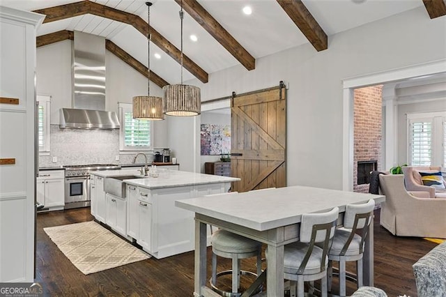 kitchen with a barn door, beamed ceiling, a kitchen island with sink, and pendant lighting