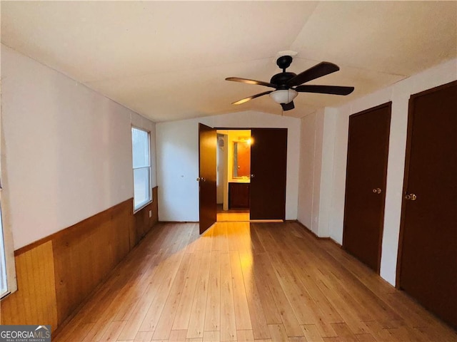 empty room with light wood-type flooring, vaulted ceiling, ceiling fan, and wooden walls