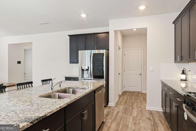 kitchen with light stone counters, sink, stainless steel appliances, light wood-type flooring, and a kitchen bar