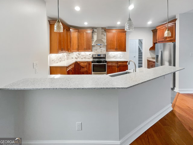 kitchen featuring light stone counters, pendant lighting, stainless steel appliances, and wall chimney range hood