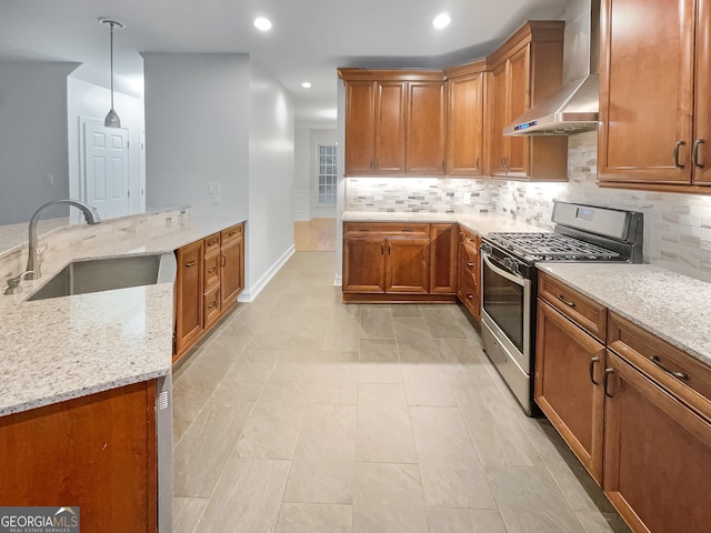 kitchen featuring gas stove, light stone counters, wall chimney range hood, and sink