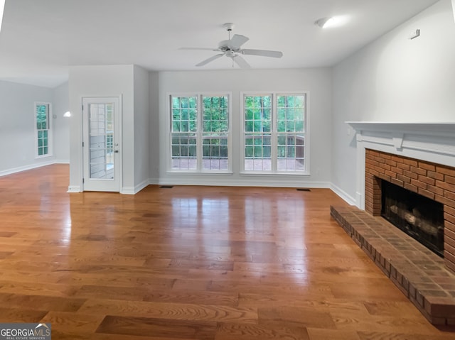 unfurnished living room with light wood-type flooring, ceiling fan, and a brick fireplace