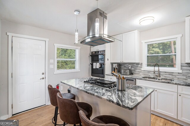 kitchen with island exhaust hood, black double oven, sink, white cabinets, and hanging light fixtures