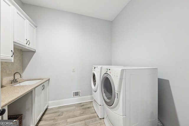 washroom featuring washing machine and dryer, cabinets, sink, and light hardwood / wood-style flooring