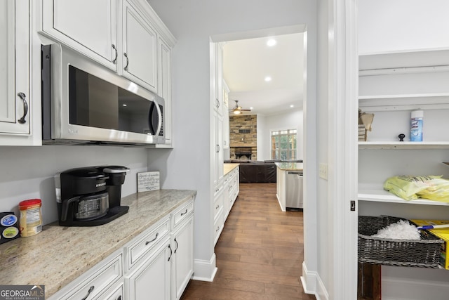 kitchen featuring stainless steel appliances, dark wood-type flooring, white cabinets, light stone countertops, and a fireplace