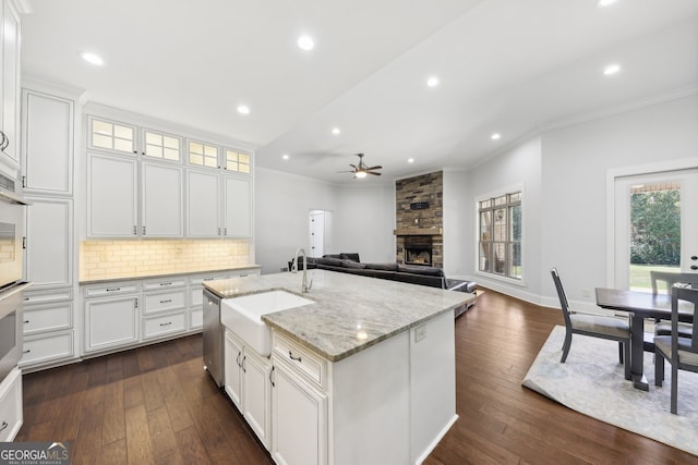 kitchen with a stone fireplace, white cabinets, sink, a kitchen island with sink, and dark hardwood / wood-style floors