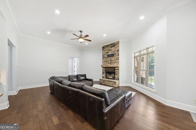 living room featuring dark wood-type flooring, a stone fireplace, ceiling fan, and crown molding