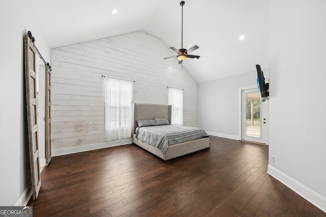 unfurnished bedroom featuring ceiling fan, high vaulted ceiling, a barn door, wooden walls, and dark wood-type flooring