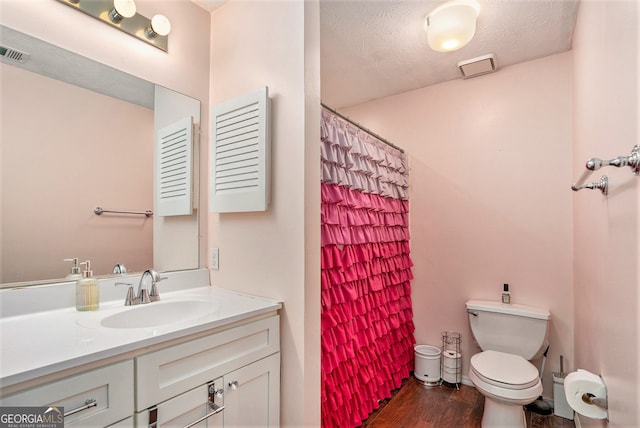 bathroom with vanity, curtained shower, a textured ceiling, hardwood / wood-style flooring, and toilet