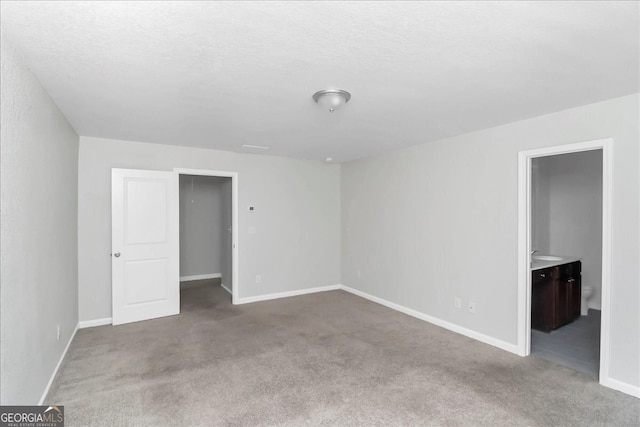 unfurnished bedroom with a textured ceiling, ensuite bathroom, carpet, and a spacious closet