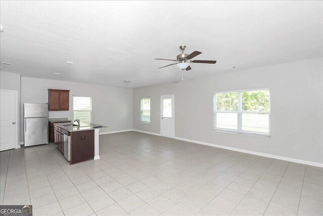 kitchen with an island with sink, light tile patterned floors, stainless steel appliances, ceiling fan, and sink