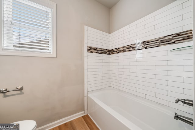 full bath with bathing tub / shower combination, toilet, wood finished floors, and baseboards