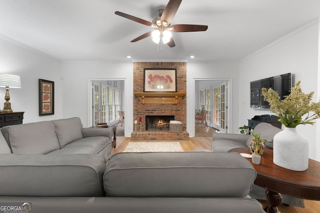 living room featuring ceiling fan, light hardwood / wood-style flooring, crown molding, and a fireplace