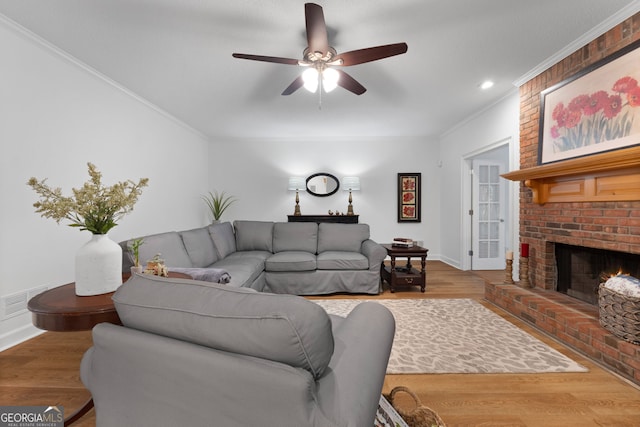 living room with a brick fireplace, ceiling fan, hardwood / wood-style flooring, and crown molding