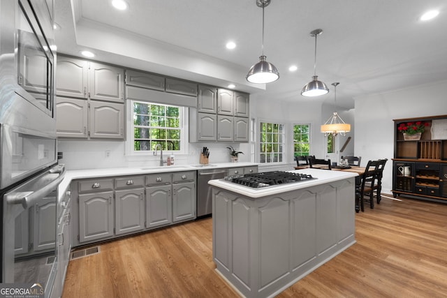 kitchen featuring gray cabinetry, hanging light fixtures, light hardwood / wood-style floors, tasteful backsplash, and appliances with stainless steel finishes