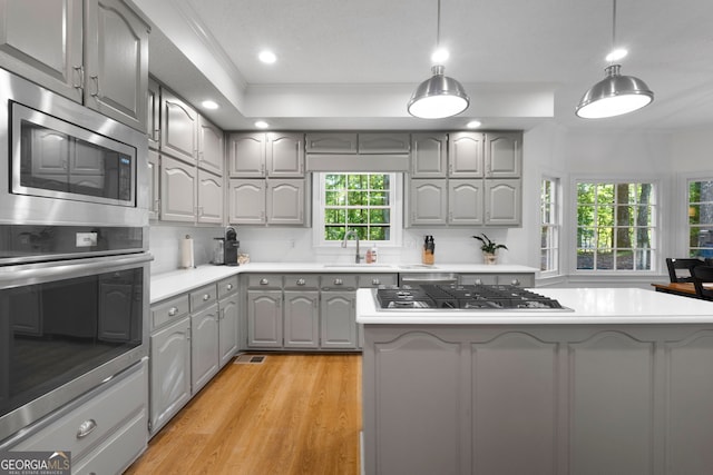 kitchen featuring appliances with stainless steel finishes, decorative light fixtures, gray cabinets, a kitchen island, and light wood-type flooring