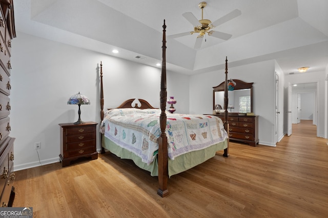 bedroom with ceiling fan, a raised ceiling, and wood-type flooring