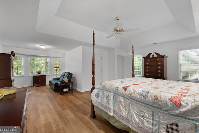 bedroom with ceiling fan, light hardwood / wood-style flooring, and a tray ceiling