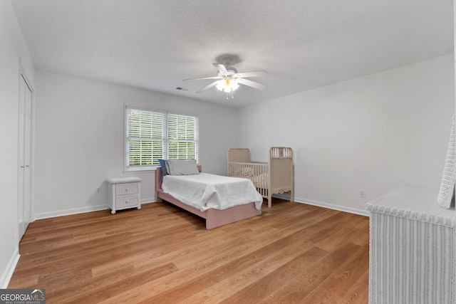 bedroom with a textured ceiling, ceiling fan, and light hardwood / wood-style floors