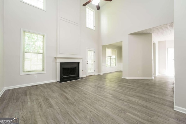 unfurnished living room featuring a high ceiling, dark hardwood / wood-style floors, ceiling fan, and a wealth of natural light