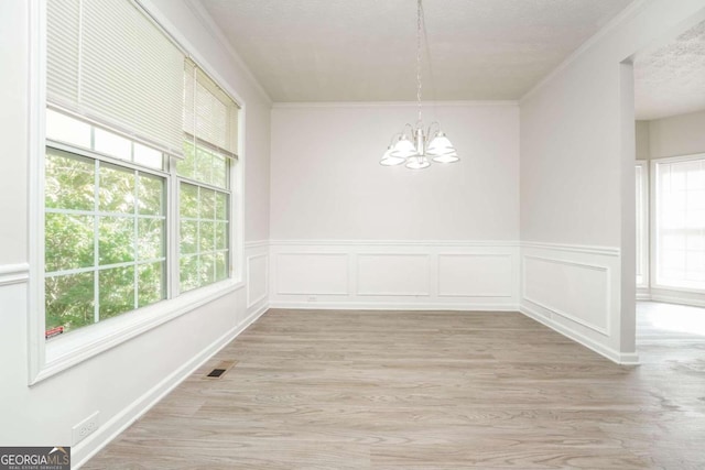 unfurnished dining area with light hardwood / wood-style flooring, a notable chandelier, ornamental molding, and a textured ceiling