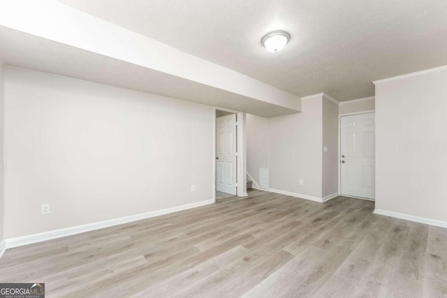 basement with a textured ceiling, light hardwood / wood-style flooring, and ornamental molding