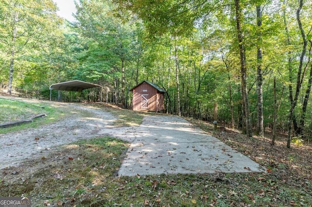 view of yard with a detached carport, driveway, a view of trees, and an outdoor structure