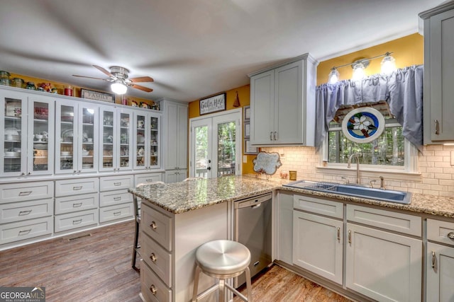 kitchen with light stone counters, light wood-type flooring, ceiling fan, stainless steel dishwasher, and sink