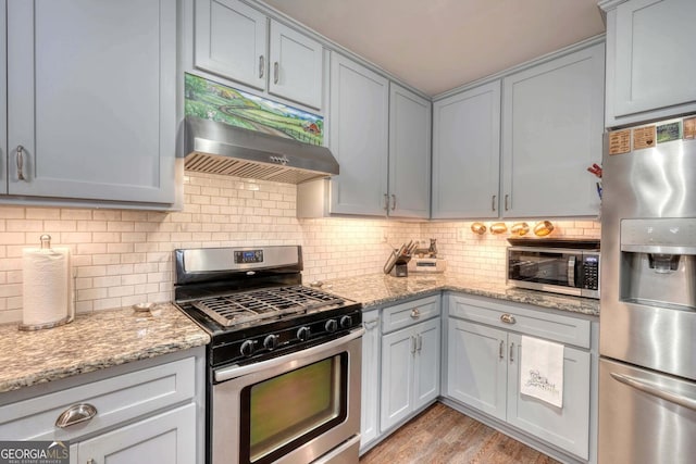 kitchen featuring backsplash, stainless steel appliances, light wood-type flooring, and light stone countertops