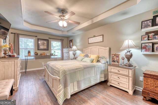 bedroom with wood-type flooring, ceiling fan, and a raised ceiling