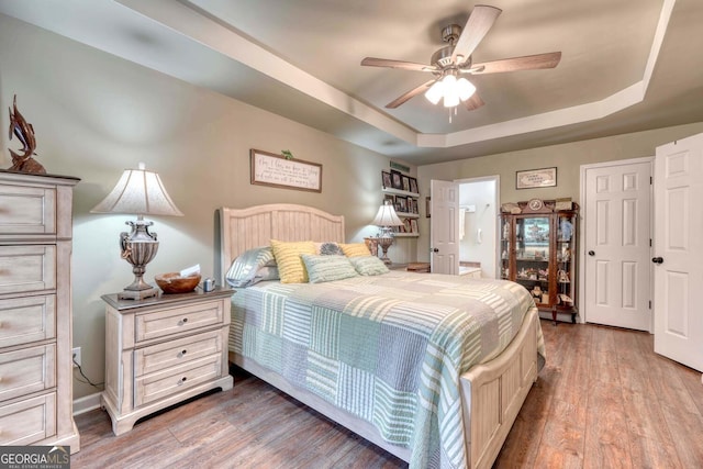 bedroom featuring ceiling fan, a tray ceiling, ensuite bathroom, and wood-type flooring