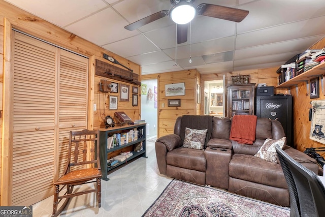 living room with a drop ceiling, wooden walls, and ceiling fan