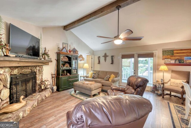 living room featuring light hardwood / wood-style flooring, vaulted ceiling with beams, ceiling fan, and a stone fireplace