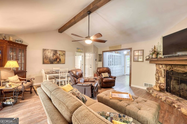 living room featuring ceiling fan, vaulted ceiling with beams, a fireplace, and light hardwood / wood-style floors