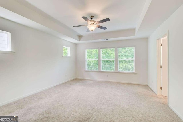 empty room featuring a tray ceiling, ceiling fan, and light colored carpet