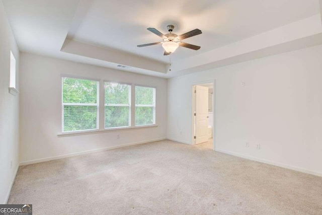 spare room with light carpet, ceiling fan, and a raised ceiling