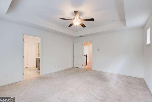 empty room with light carpet, a tray ceiling, and ceiling fan