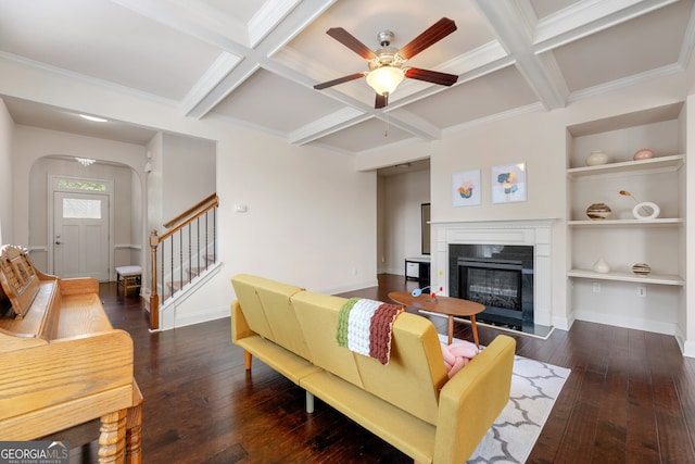 living room with coffered ceiling, built in shelves, dark hardwood / wood-style floors, ceiling fan, and beam ceiling