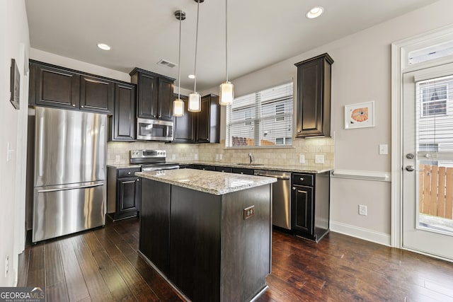 kitchen featuring appliances with stainless steel finishes, backsplash, a kitchen island, and hanging light fixtures