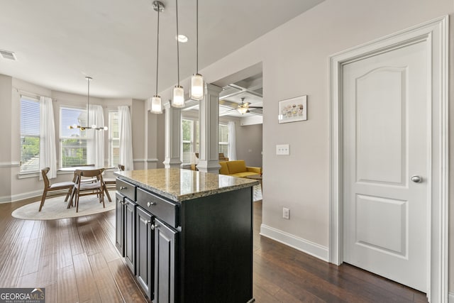 kitchen with light stone countertops, ceiling fan, dark wood-type flooring, a center island, and hanging light fixtures