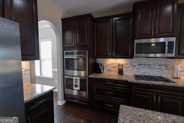 kitchen with light stone countertops, decorative backsplash, dark hardwood / wood-style flooring, appliances with stainless steel finishes, and dark brown cabinetry