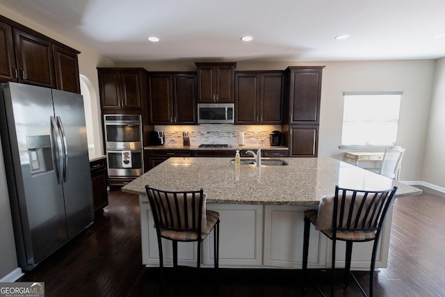 kitchen featuring stainless steel appliances, a kitchen island with sink, decorative backsplash, and dark wood-type flooring