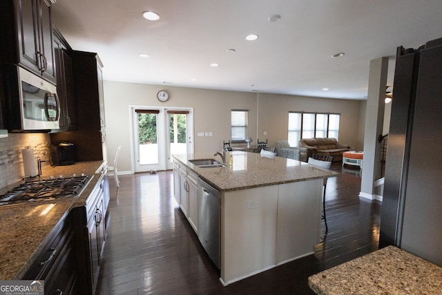 kitchen featuring stainless steel appliances, an island with sink, decorative backsplash, a breakfast bar area, and dark brown cabinets