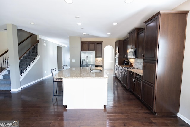 kitchen with light stone countertops, a center island with sink, tasteful backsplash, dark hardwood / wood-style flooring, and appliances with stainless steel finishes