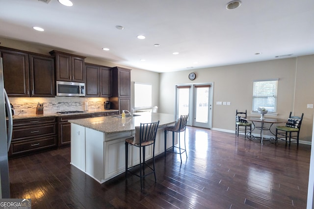 kitchen featuring a breakfast bar area, a center island with sink, stainless steel appliances, decorative backsplash, and sink