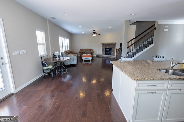 kitchen featuring sink, a fireplace, white cabinetry, light stone counters, and dark hardwood / wood-style flooring